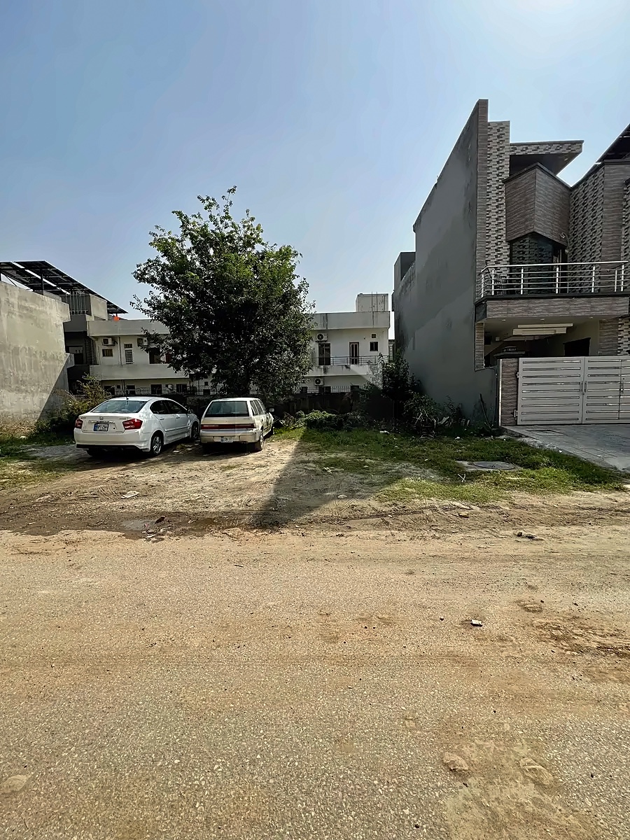 Client-supplied street-front photograph of the D-12 residential plot between neighbouring houses